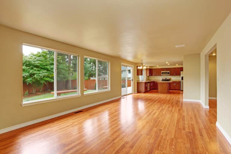 Empty house interior with new hardwood floor. Spacious empty living room with exit to backayrd area and kitchen area